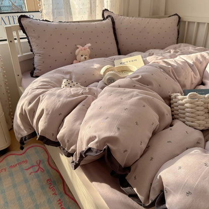Mauve bow print bedding set with charcoal ruffle edges on a cream bed frame