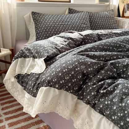 Charcoal Daisy floral ruffle bedding set with white lace trim styled on a bed