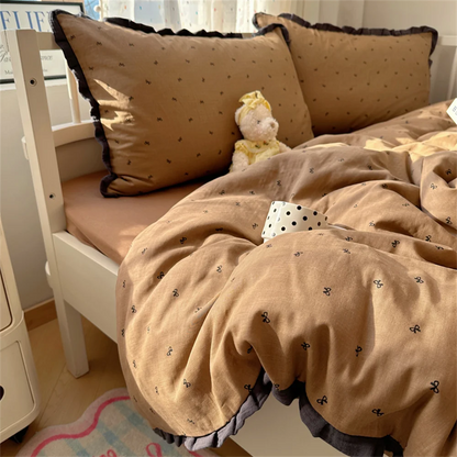 Caramel bow print bedding set with dark charcoal ruffle trim on a white wood bed