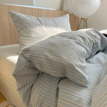 Light blue and gray striped cotton bedding set on a sunlit bed with soft pillows