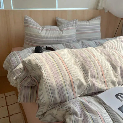 Striped cotton bedding in pastel grey, lilac, and blush tones on a minimal wooden bed