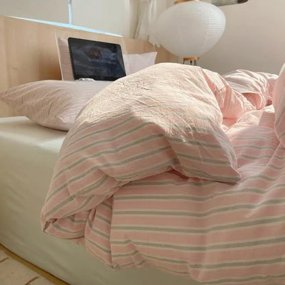 Pink striped bedding with soft blush tones and light gray accents on a cozy bed in morning light